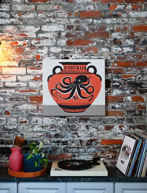 This design includes a large octopus depicted on an ancient clay vase, accented by unique marks and patterns. The art print is displayed in a modern and eclectic home.