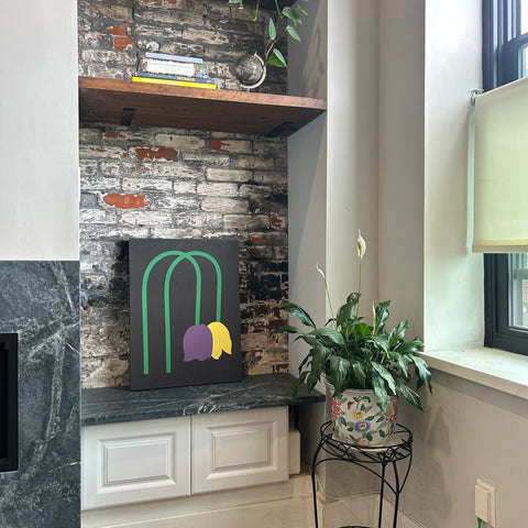 A piece of canvas artwork featuring a black background with green lines and purple and yellow shapes depicting wilted tulips displayed in a modern home setting.