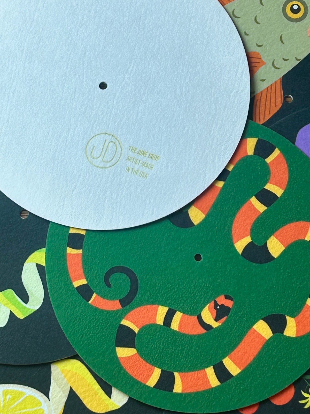 Pile of colorful, illustrative slipmats with one upside down to show logo and "Artist-made in USA" etching