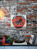 This design includes a large octopus depicted on an ancient clay vase, accented by unique marks and patterns. The art print is displayed in a modern and eclectic home.