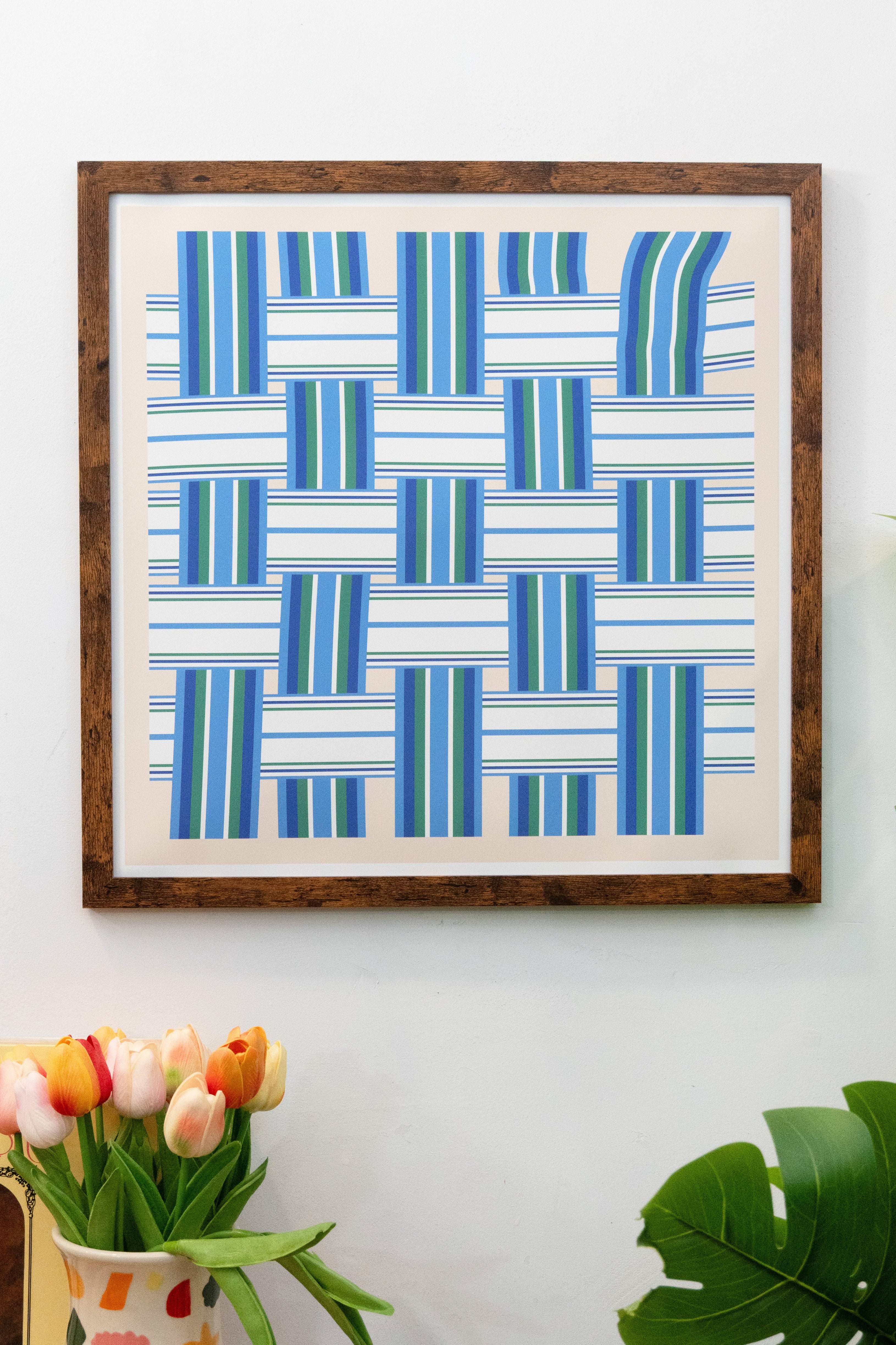 Framed blue and green geometric lawn chair pattern print with horizontal and vertical lines on a beige background with white border displayed on a white wall