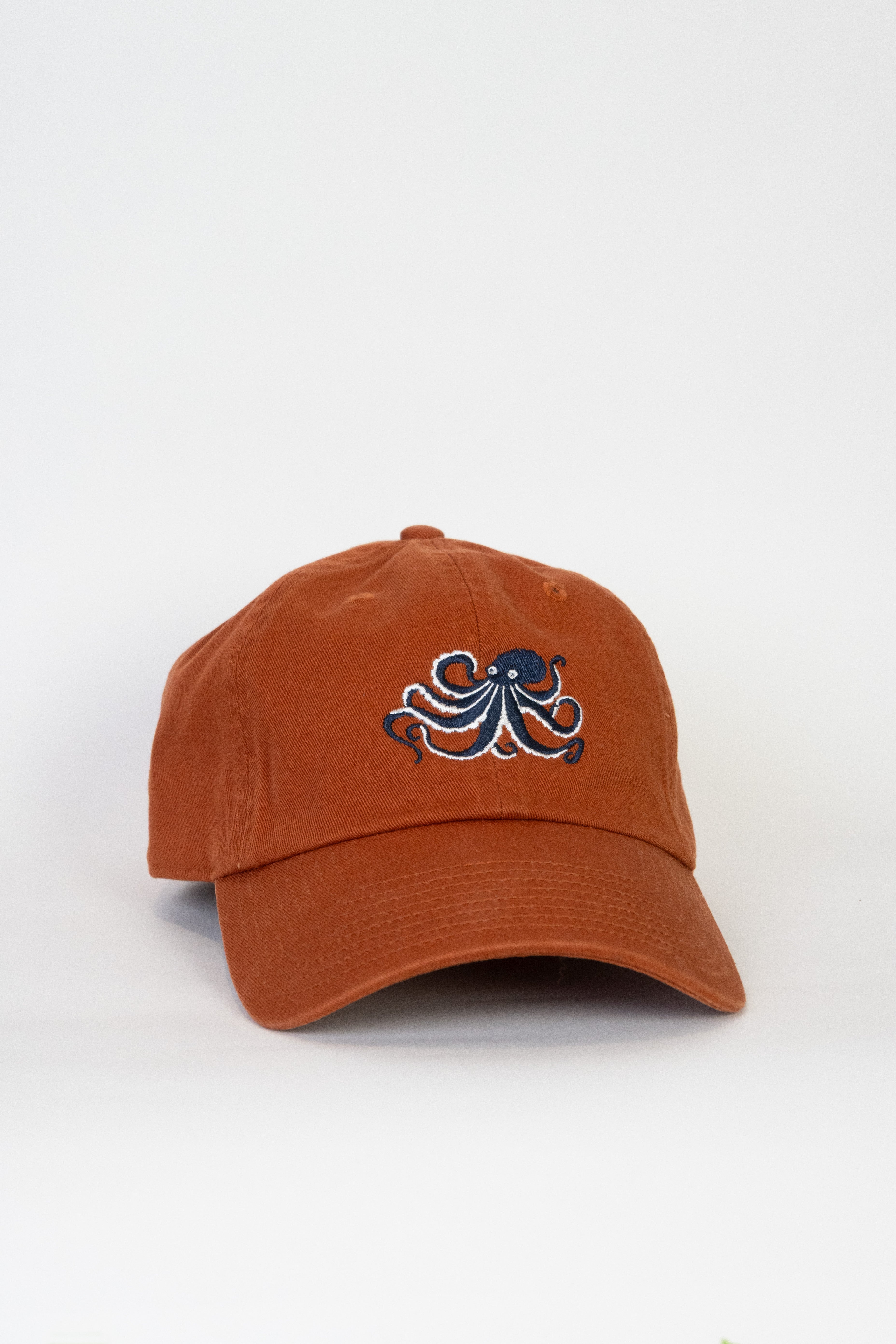 Burnt orange baseball cap with an embroidered octopus design on a white background