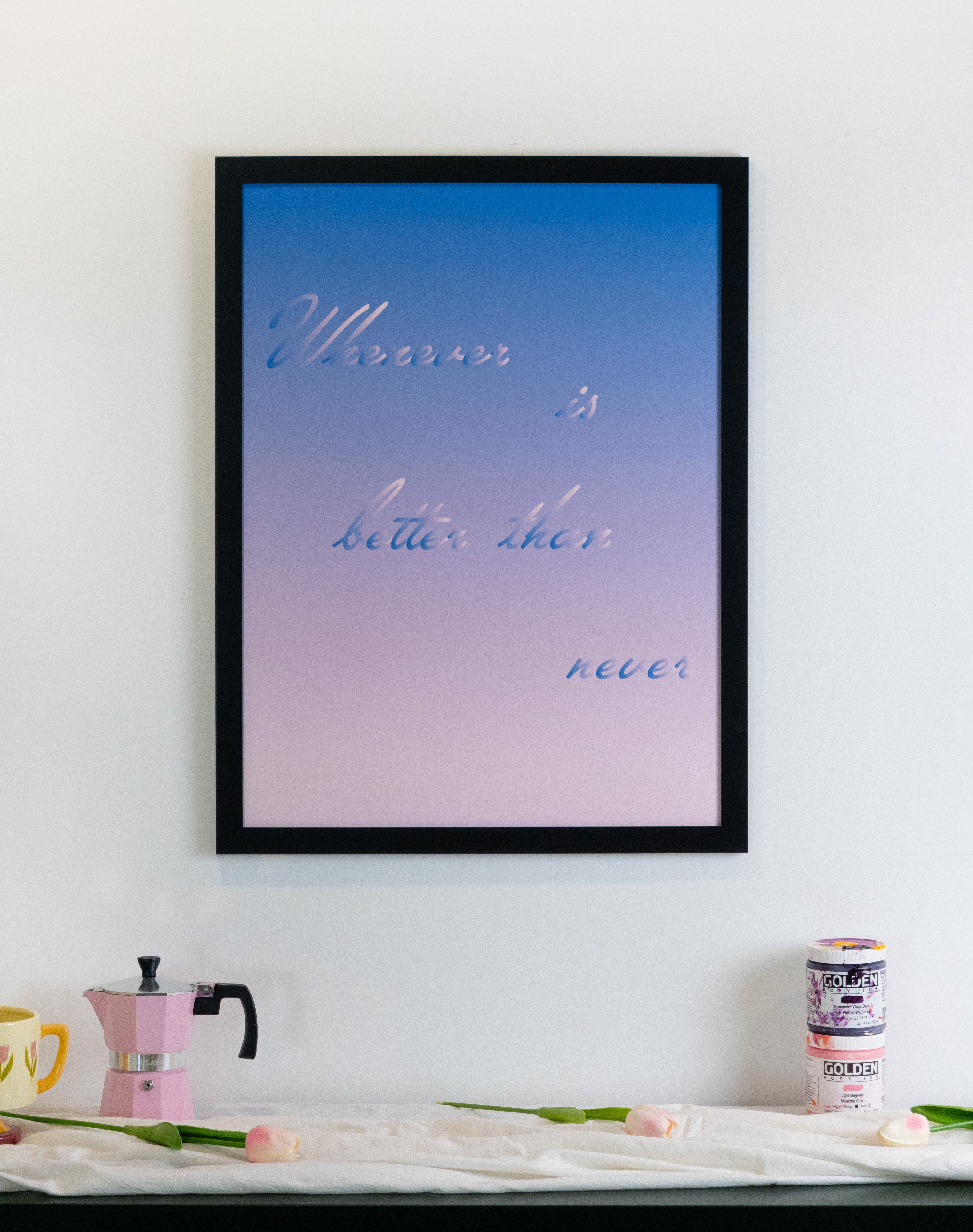 Framed artwork with a blue and pink gradient background and text on a wall above a table with decor items.