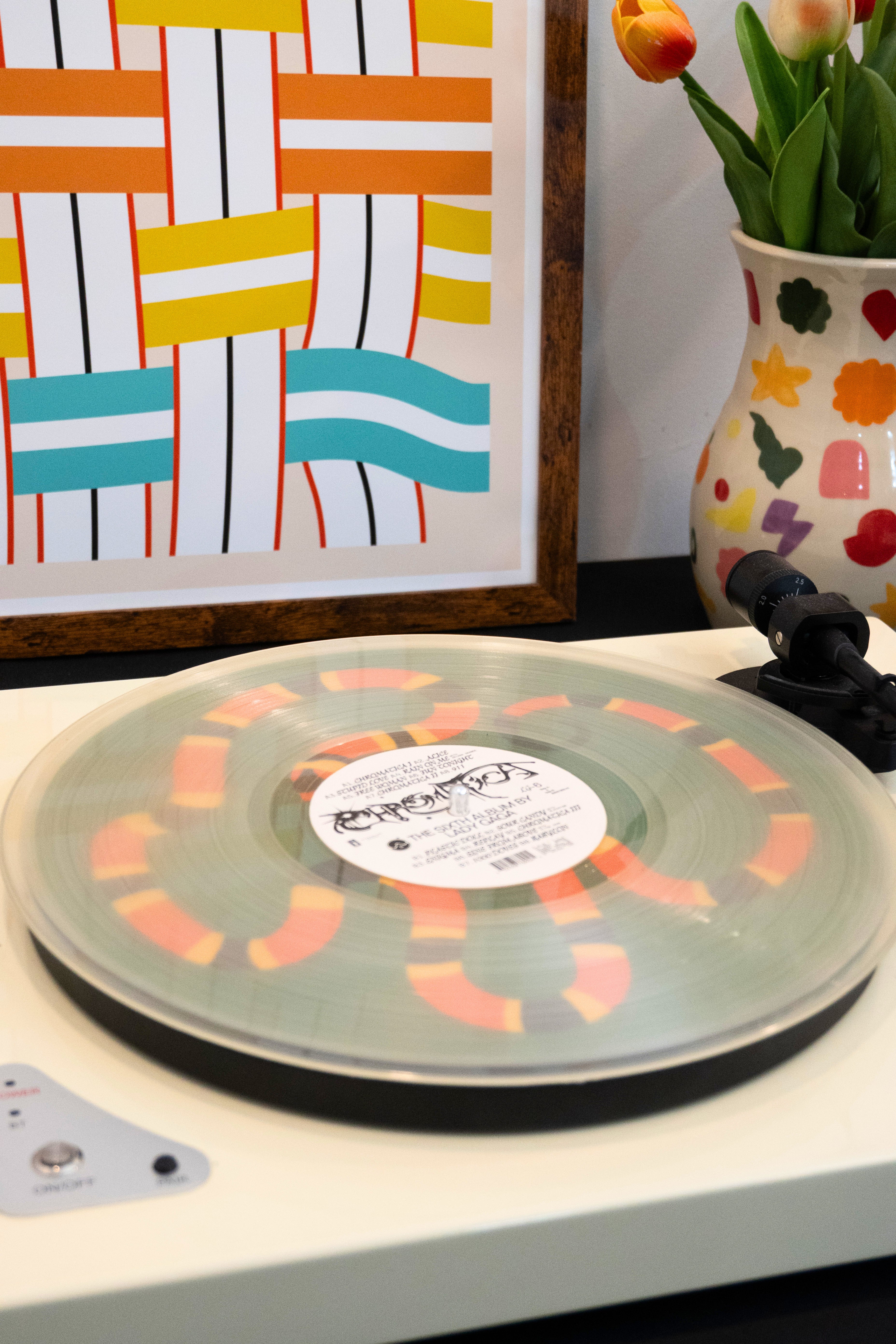 Transparent vinyl record on a turntable above a colorful snake slipmat with abstract painting and vase in the background