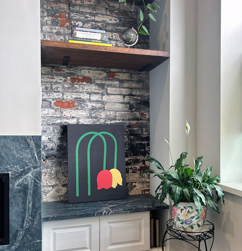 A piece of canvas artwork featuring a black background with green lines and red and yellow shapes depicting wilted tulips displayed in a modern home setting.