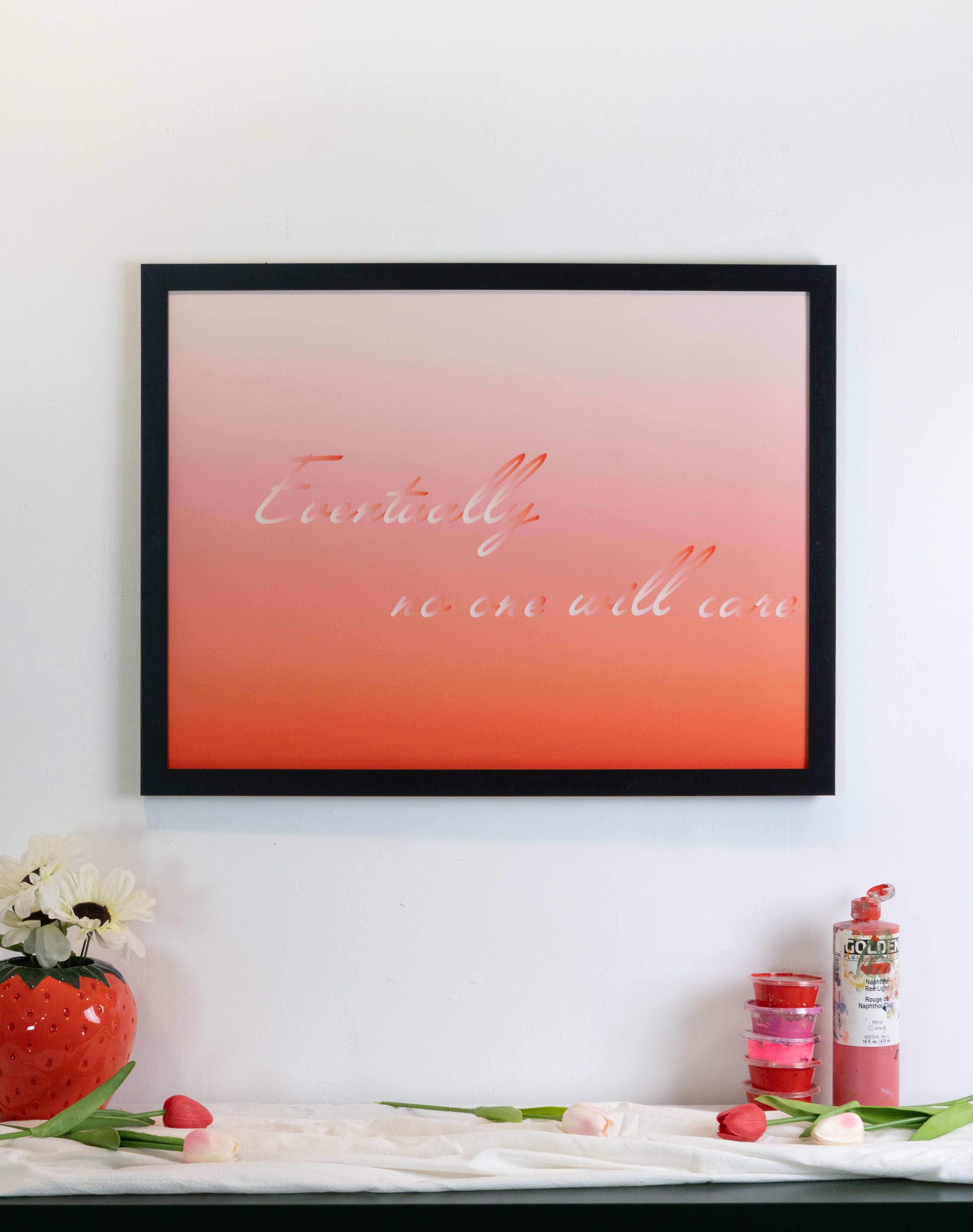 Framed artwork with a red gradient background and text on a white wall with decorative items.