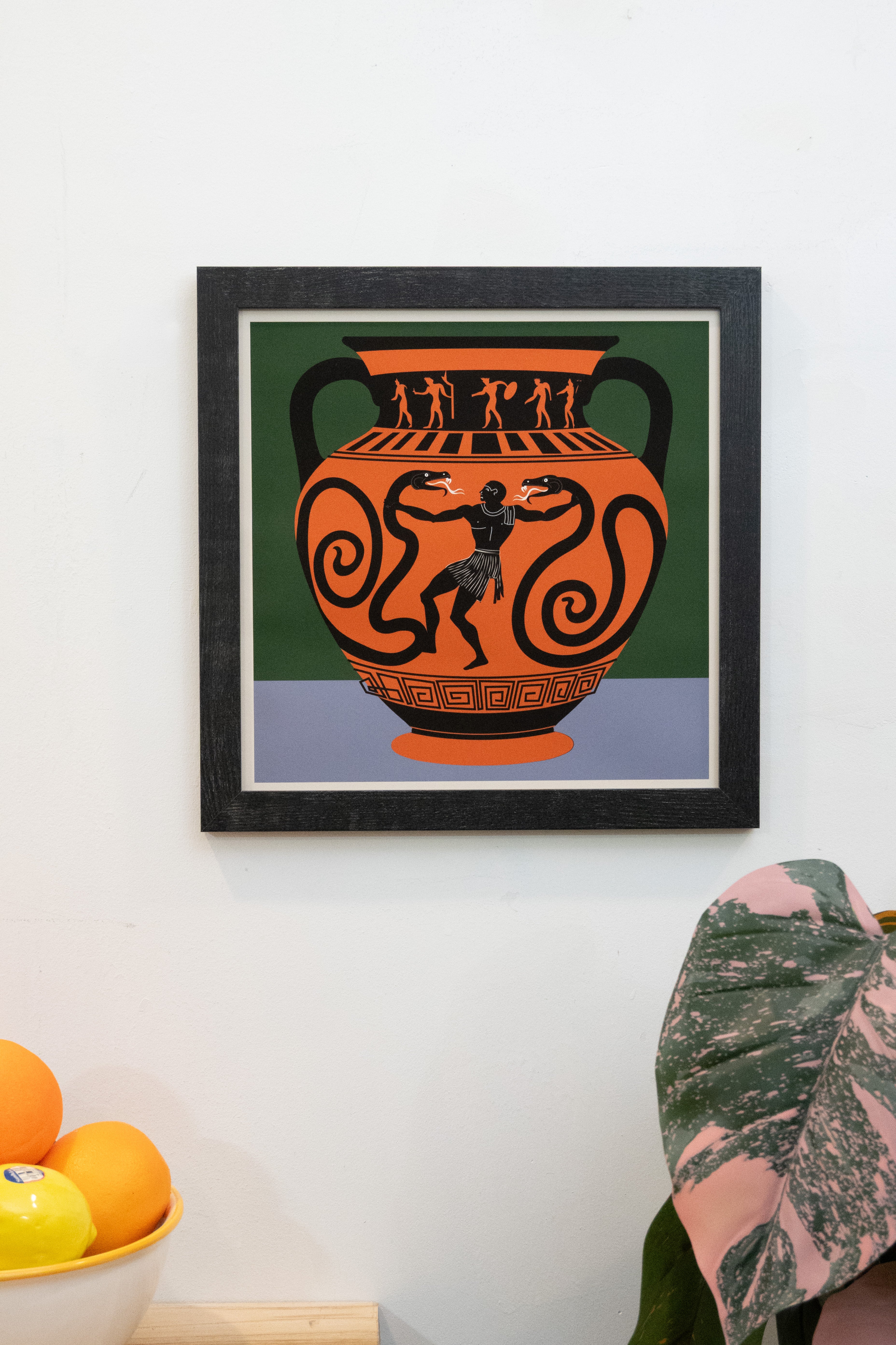 Framed art print with heroic "man with snakes" ancient vase design with with periwinkle and forest green background with white border displayed on a whtie wall
