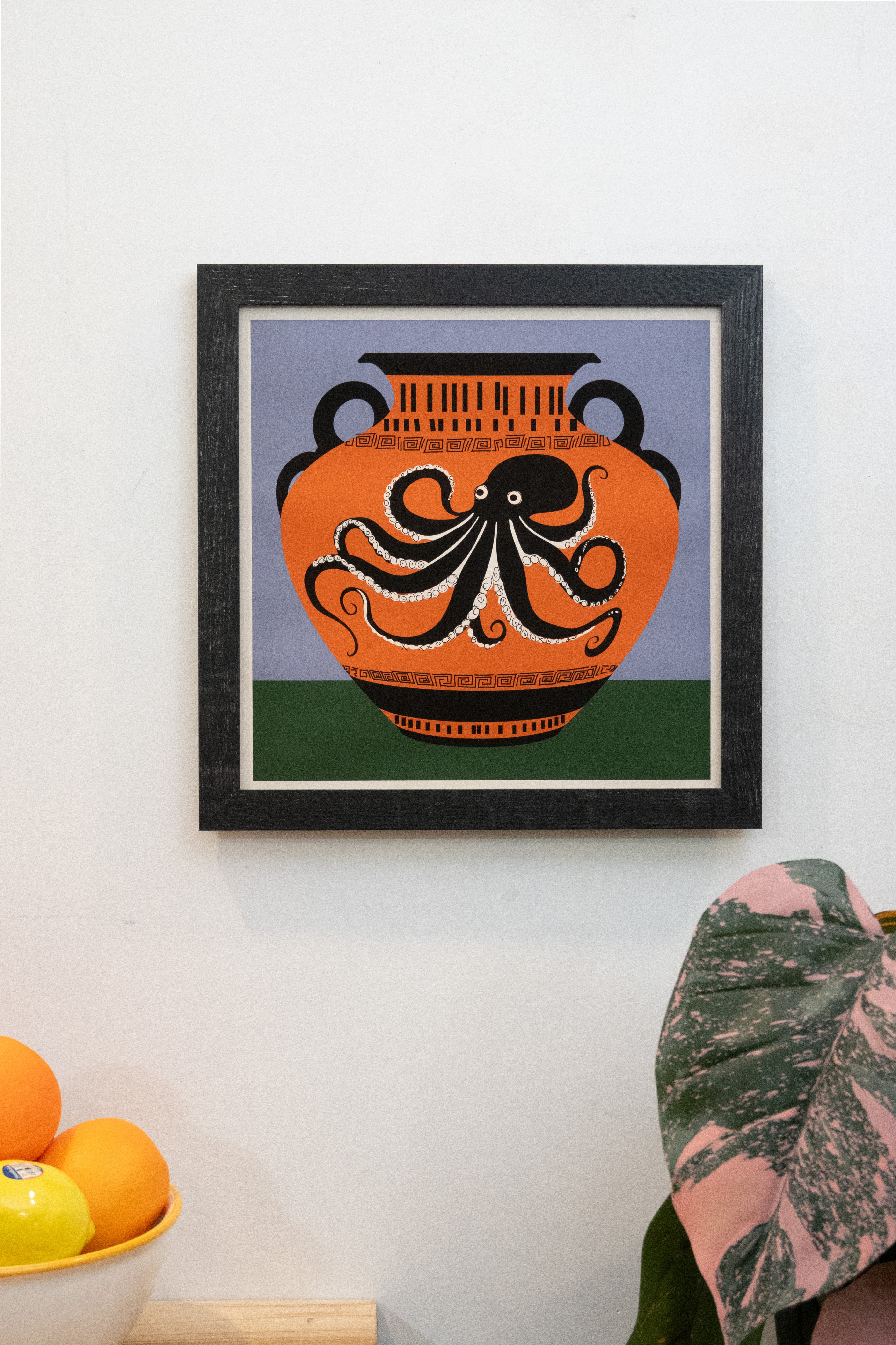 Framed art print with octopus vase design with with periwinkle and forest green background with white border displayed on a wall