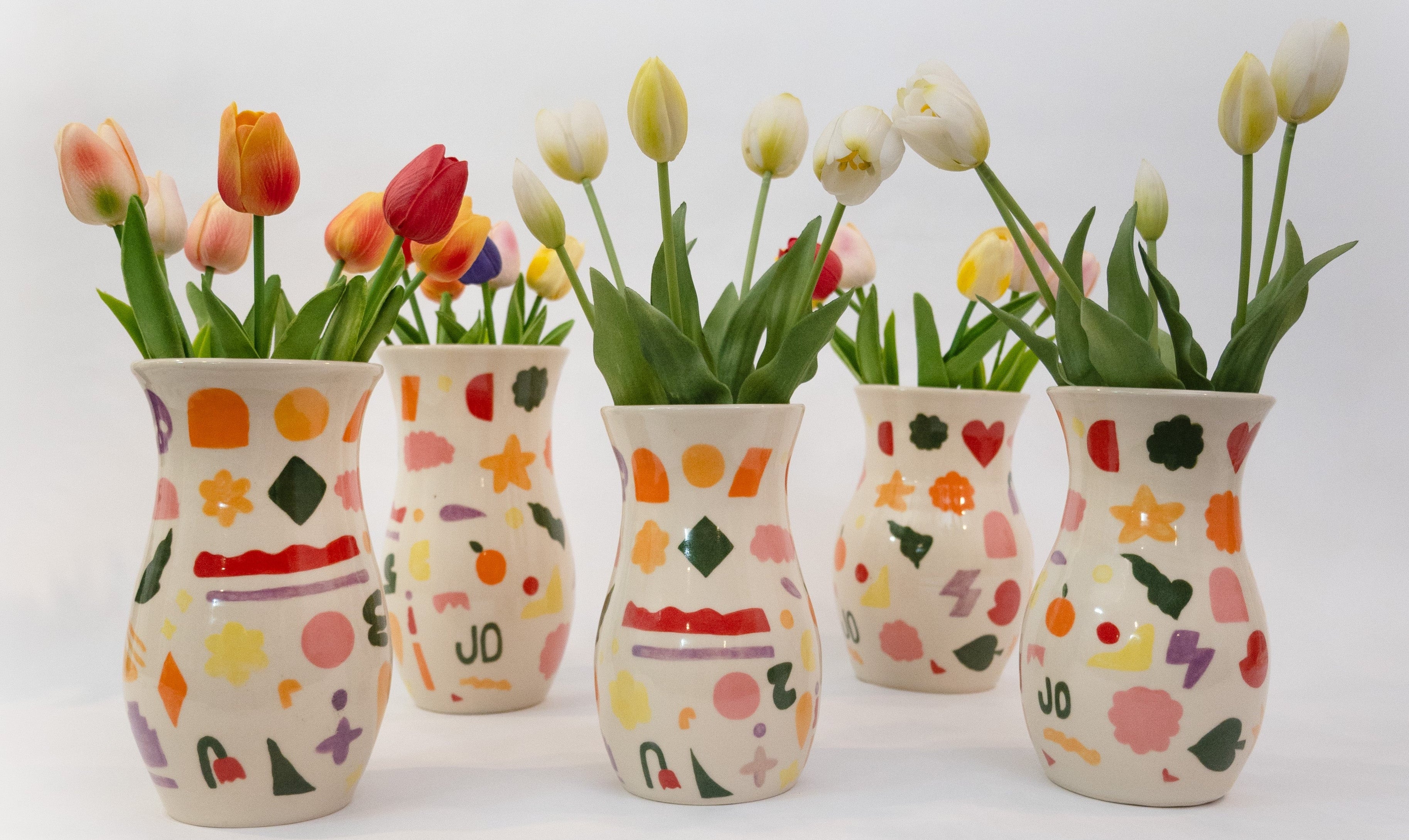 Five ceramic vases with colorful patterns filled with tulips on a white background