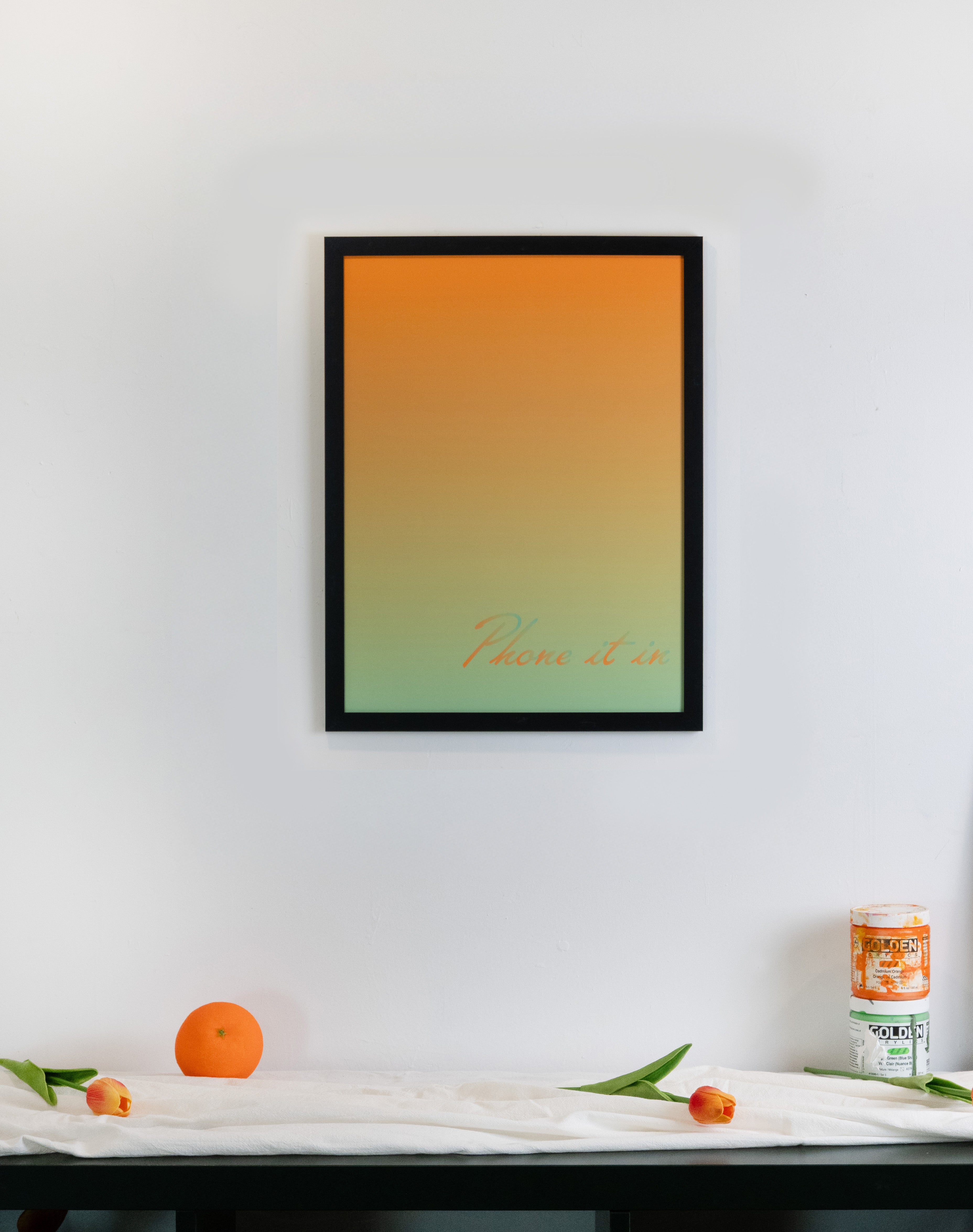 Framed artwork with green and orange gradient design and text on a white wall above a table.