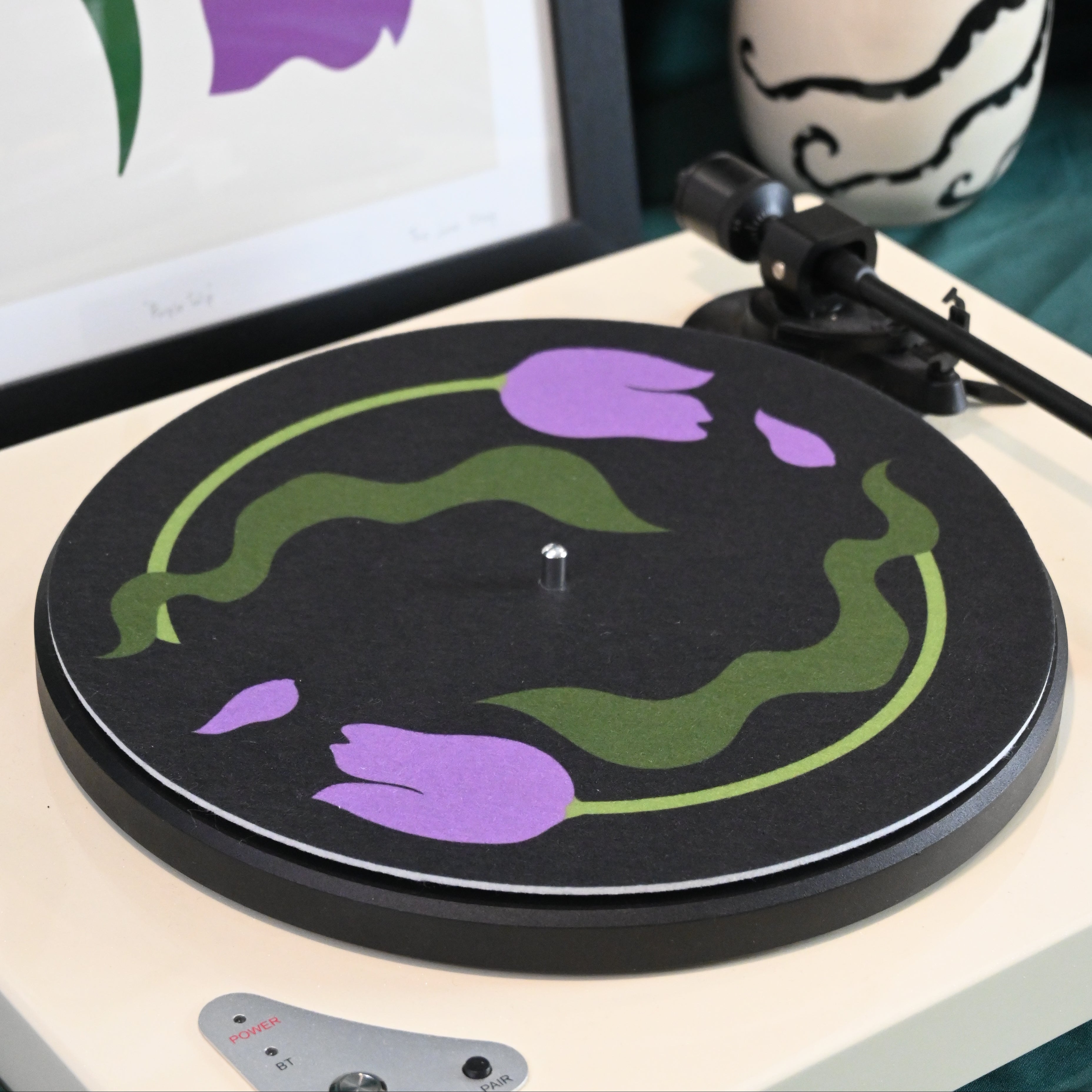 Vinyl record player slipmat with a floral purple tulip design on a black background - shown with styled objects and art