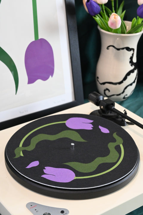 Vinyl record player slipmat with a floral purple tulip design on a black background - shown with styled objects and art