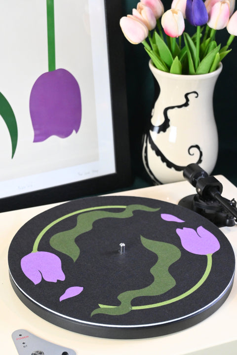 Vinyl record player slipmat with a floral purple tulip design on a black background - shown with styled objects and art