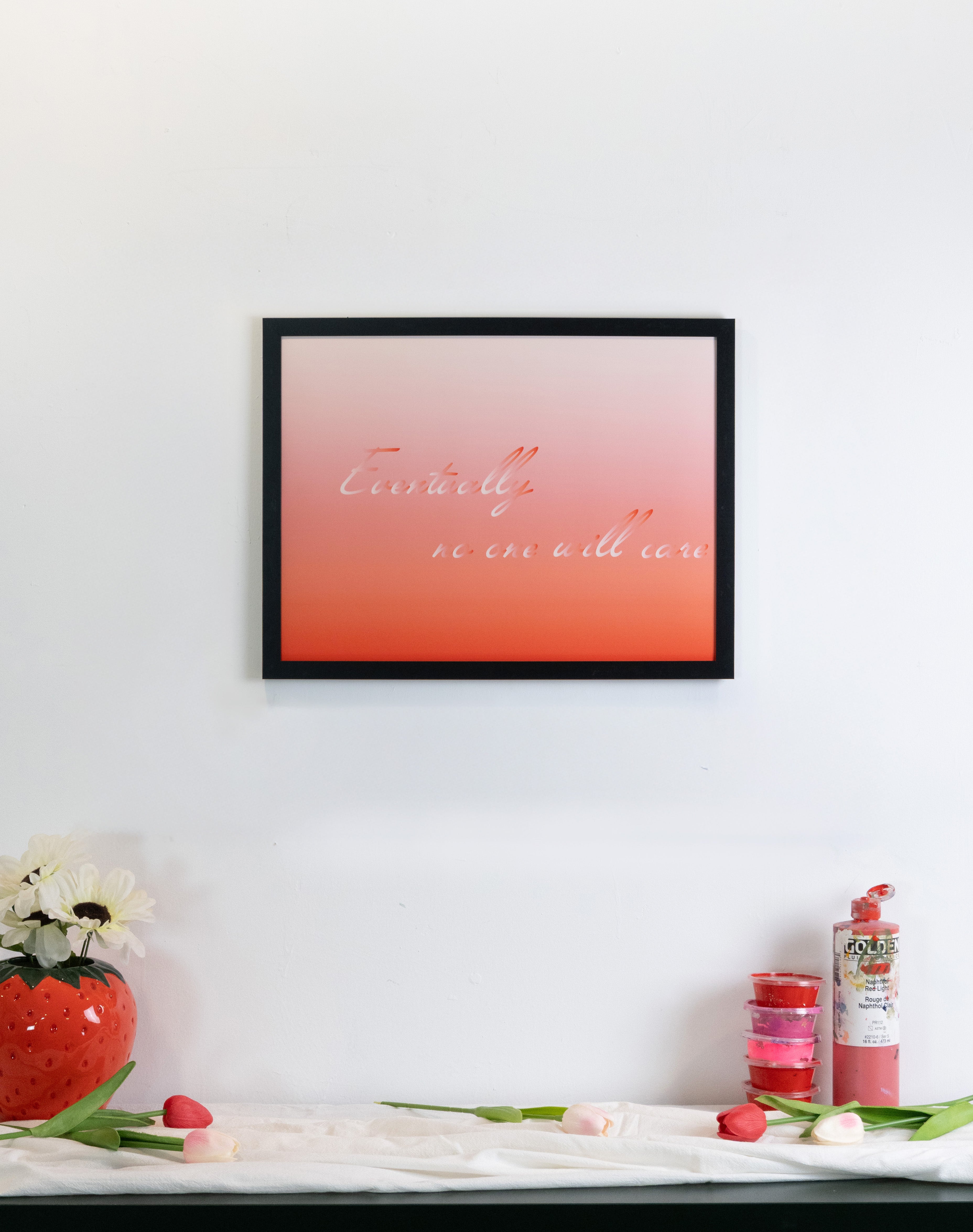 Framed artwork with a gradient design on a white wall above a shelf with decorative items.
