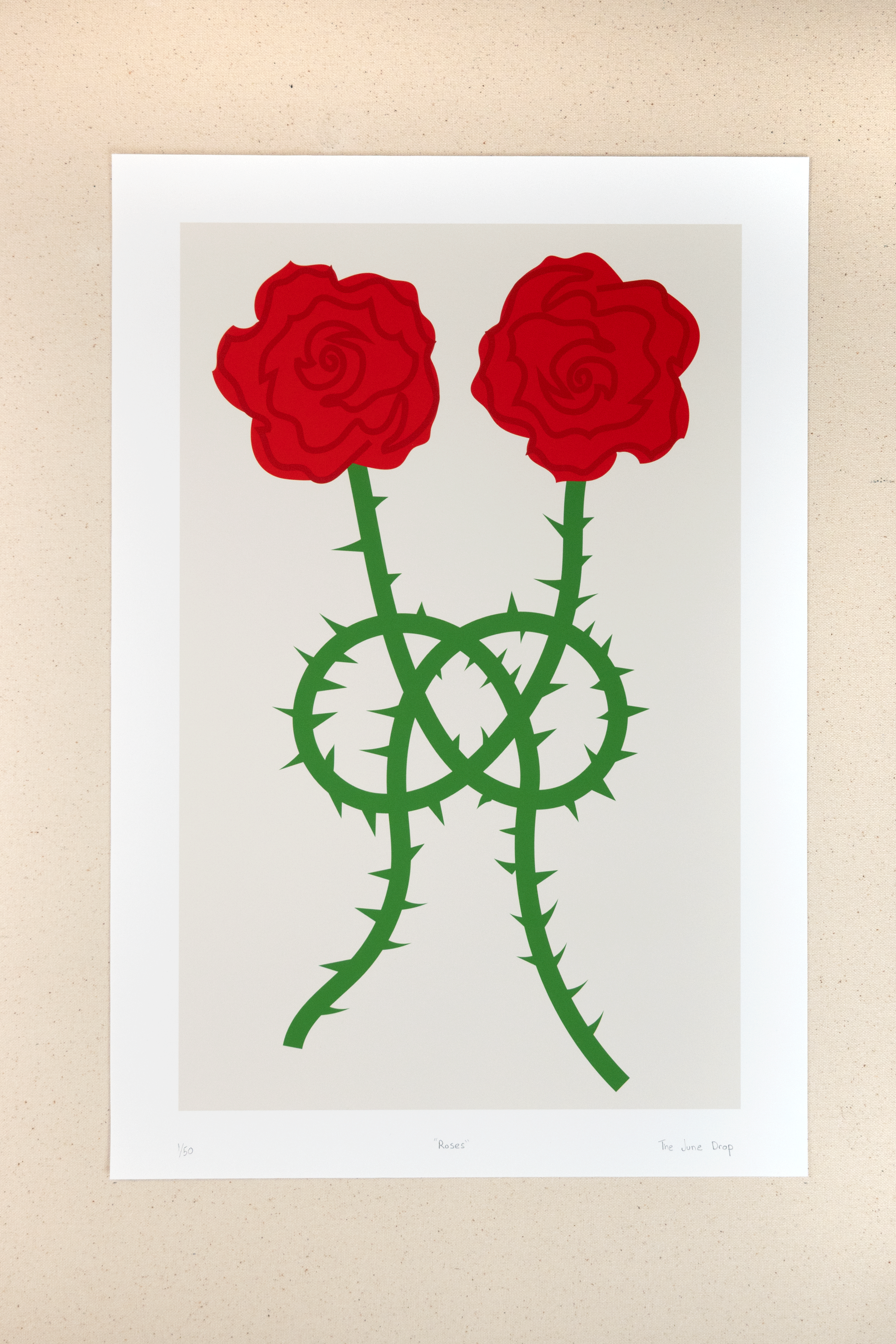 Minimal print design with red roses and green prickly stems tied in a knot over an off-white background