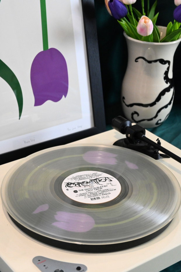 Vinyl record player slipmat with a floral purple tulip design on a black background - shown beneath a transparent record - styled with artisan objects and art