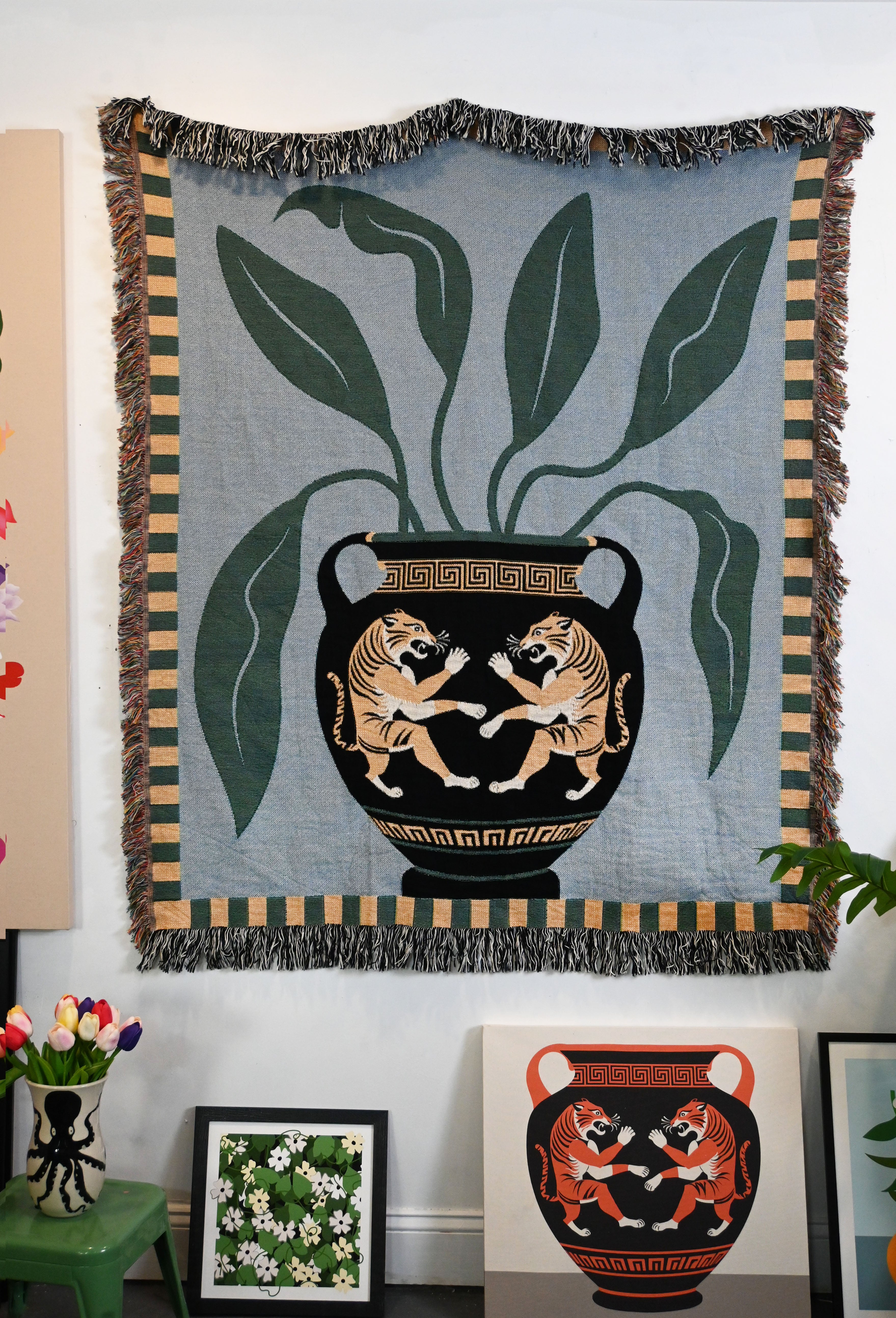 Woven blanket with a tiger and leaves design on a large vase, hanging on a wall. Multicolor, artist-drawn