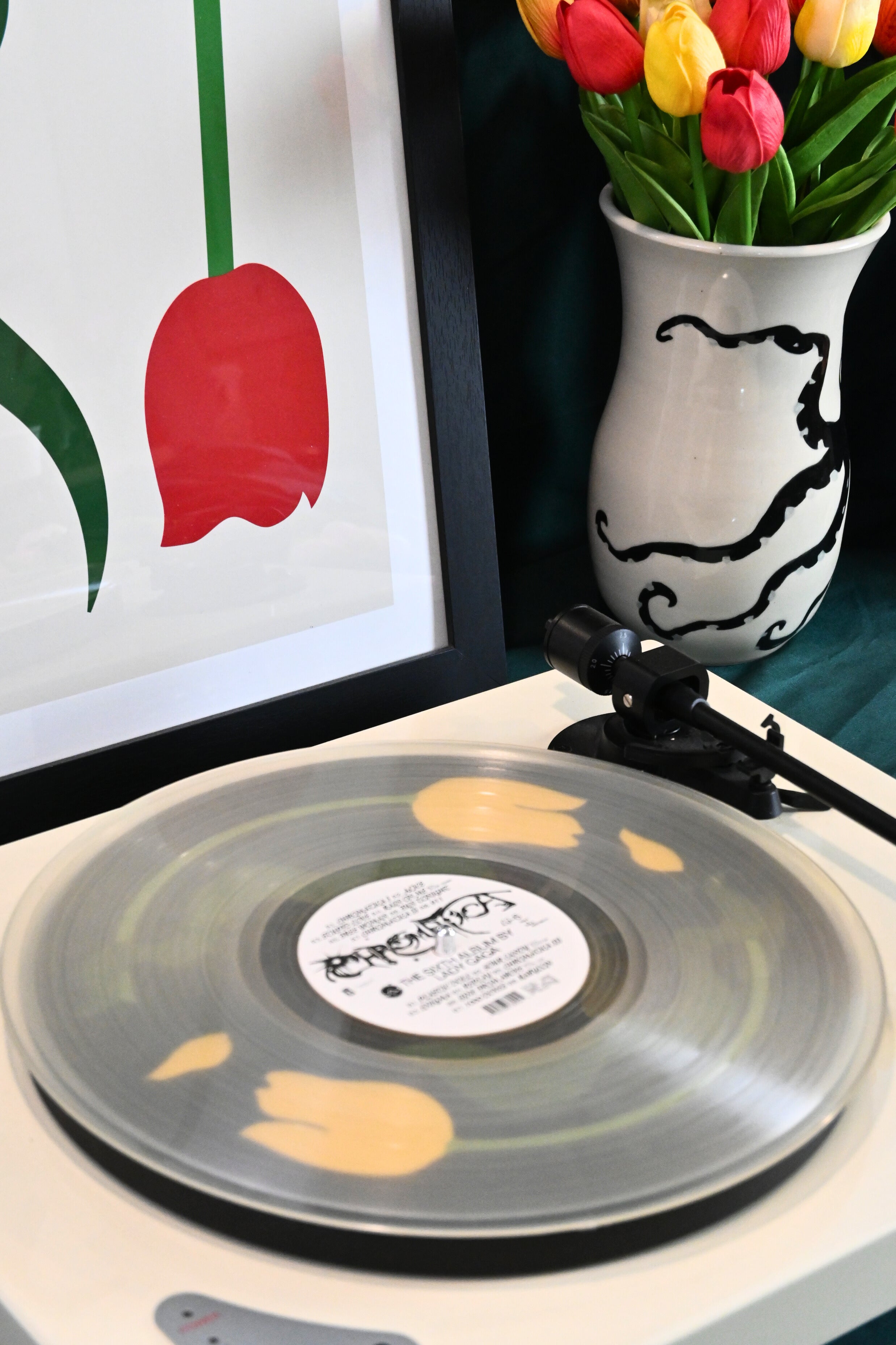 Vinyl record player slipmat with a floral yellow tulip design on a black background - shown beneath a transparent record - styled with artisan objects and art