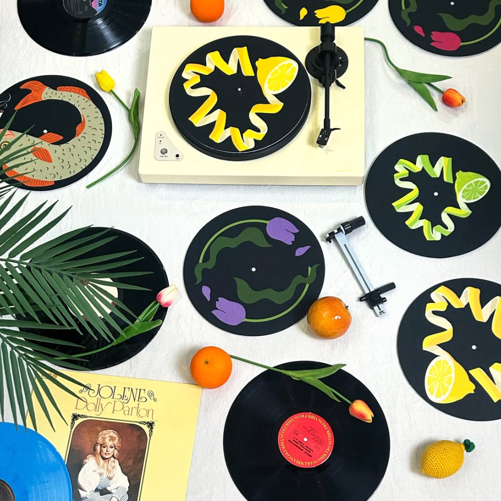 Colorful decorative vinyl records and slipmat accessories with artistic designs on a white surface with a record player.
