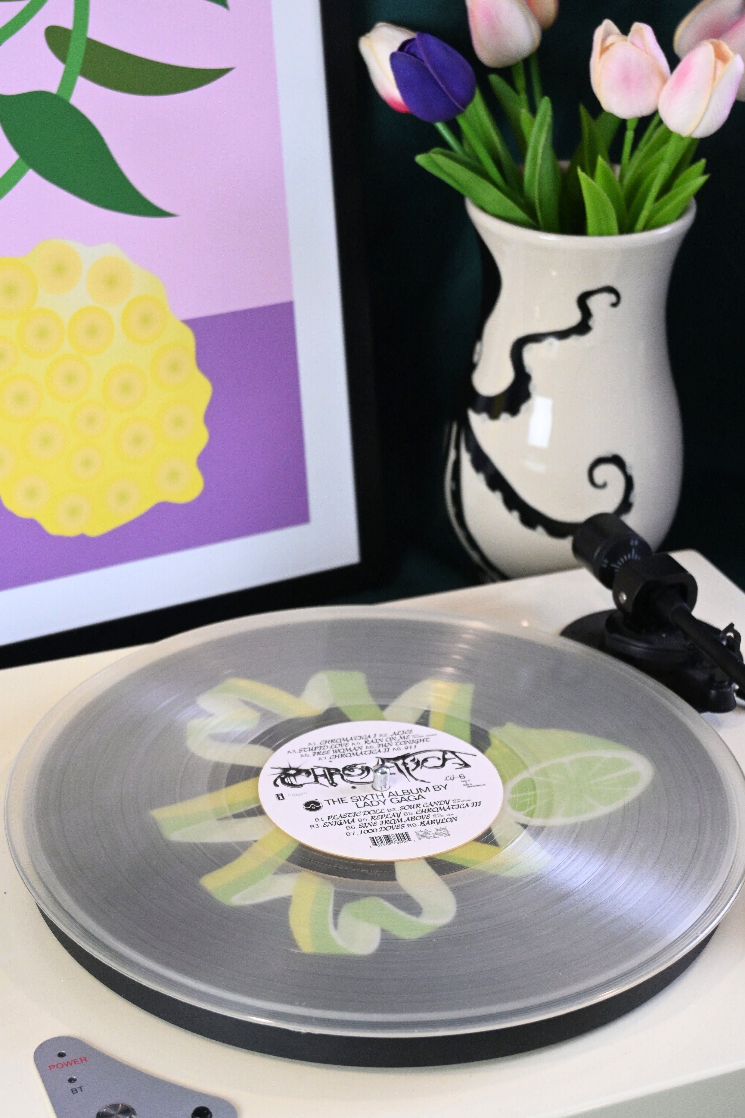 Vinyl record player slipmat with a green lime twist graphic design on a black background - shown beneath a transparent record - styled with artisan objects and art