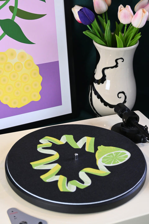 Vinyl record player slipmat with a graphic green lime citrus design on a black background - shown with styled objects and art