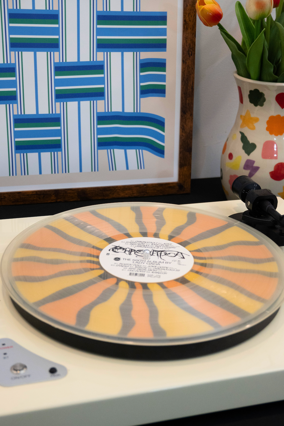 Colorful sunburst design vinyl record player slipmat on a turntable below a transparent record - with eclectic vase and art in the background