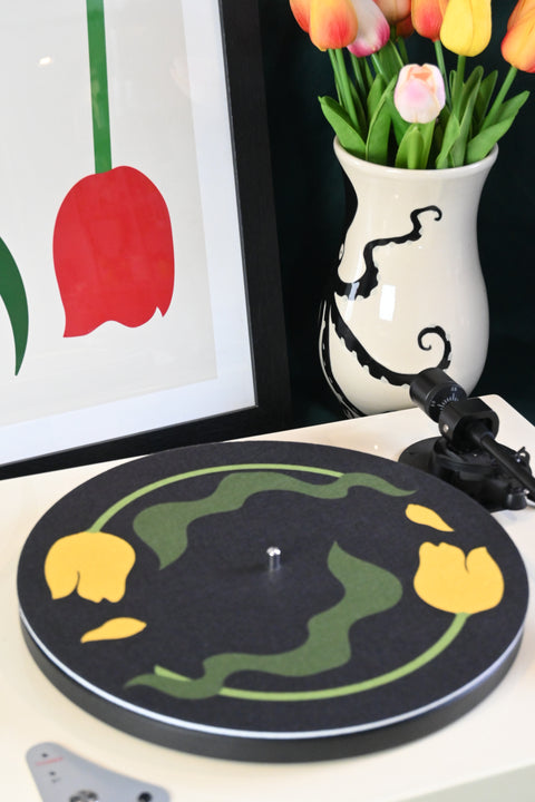 Vinyl record player slipmat with a floral yellow tulip design on a black background - shown with styled objects and art